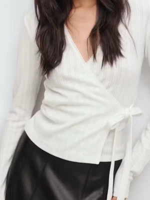 Vit omlottopp med knytband - Snygg vit omlottopp med långa ärmar och knytband i sidan. Toppen har v-ringning och är tillverkad i ett ribbat material som ger en stilren och fräsch look. Perfekt att styla med både jeans och kjol.