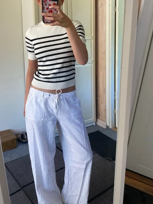 Vit och svart randig topp - Vit topp med svarta horisontella ränder och rund hals. Modellen är croppad och har korta ärmar. Perfekt för en stilren och avslappnad look. Materialet känns mjukt och stretchigt, troligen bomull eller en bomullsblandning.