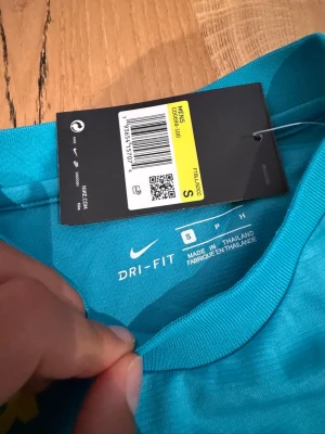 Turkos Nike Dri-FIT träningströja Brasilien  - Säljer en turkos träningströja från Nike med Dri-FIT-material som håller dig torr under träningen. Tröjan har gul Nike-logga och trycket 'Itau' på bröstet. Perfekt för sport eller gympass och har en klassisk rund hals.