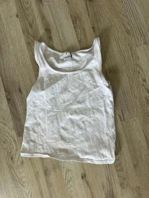 Vit ärmlös linnetopp - Klassisk vit linnetopp i bomull med rund halsringning och breda axelband. Perfekt att styla till jeans eller kjol för en enkel och clean look. Tillverkad i Turkiet.