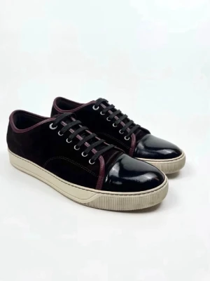 Lanvin  - Stilrena svarta sneakers med glansig lackad tå och mörklila detaljer längs kanterna. Ovandelen är i mocka och sulan är vit och platt. Skorna har svarta snören och metallfärgade öljetter för en clean look.