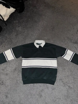 Långärmad polotopp - Långärmad polotopp med breda svarta och vita ränder, klassisk krage och en baggy passform. Tillverkad i mjukt bomullsmaterial för extra komfort. Köptes för 750, pris kan diskuteras.