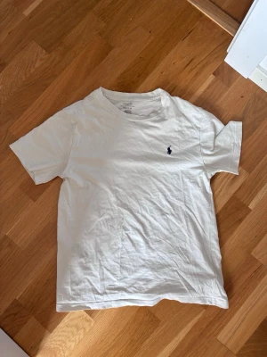 Vit t-shirt från Polo Ralph Lauren - Klassisk vit t-shirt från Polo Ralph Lauren med den ikoniska lilla loggan broderad på bröstet. T-shirten är i storlek 150cm och passar dig om du är ca 148-162cm