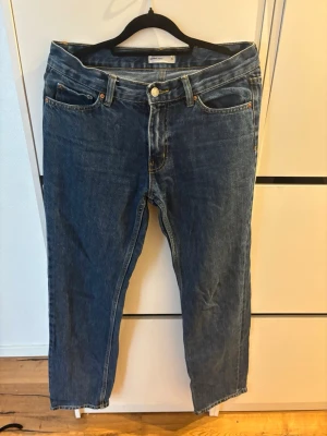 Blå raka jeans  - Klassiska blå jeans i rak modell med fem fickor och gylf med knapp. Jeansen har normalhög midja och tydliga sömmar i kontrastfärg. Tillverkade i denim, perfekt för en avslappnad och tidlös stil.