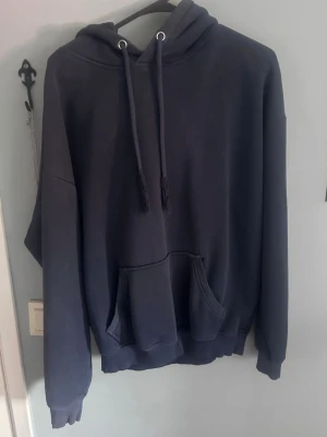 Mörkblå oversized hoodie med huva - Säljer en mörkblå oversized hoodie med stor känguruficka framtill och justerbar huva med dragsko. Hoodien har ribbade muddar vid ärmslut och nederkant. Perfekt för en chill och avslappnad stil.