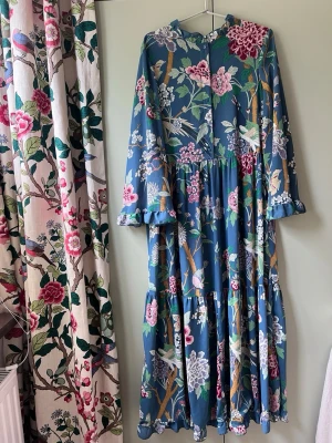 Blommig långklänning h&m x Gpj Baker  - Långklänning med blå bas och färgglatt blommönster i rosa, vitt, grönt och lila. Klänningen har långärmade, lösa ärmar och volangdetaljer vid ärmslut och kjol. Tillverkad i ett lätt och mjukt material, perfekt för sommar eller vår.
