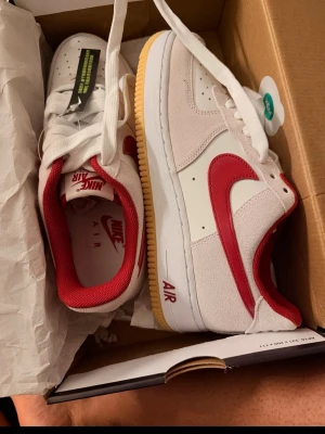 Nike Air Force 1 vita/röda sneakers - Säljer ett par Nike Air Force 1 i vit/röd färg. Helt nya och aldrig använda eftersom de tyvärr var för stora. Kommer med originalkartong. Skicket är perfekt. Skickas snabbt eller kan hämtas. 