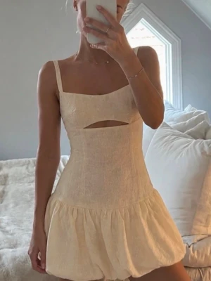 Ljus kort klänning med cut-out - Superfin ljus kort klänning med smala axelband och cut-out detalj under bysten. Klänningen har en volangig kjol och är tillverkad i ett lätt material som känns perfekt för varma dagar.