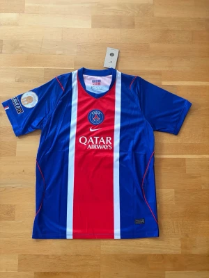 PSG matchtröja O. Dembélé #10 - Snygg blå PSG matchtröja från Nike med röd och vit mittpanel, Qatar Airways-logga och klubbmärke på bröstet. På ryggen står O. Dembélé och nummer 10. 