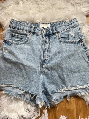 Ljusblåa jeansshorts - Säljer ett par ljusblåa jeansshorts från HM med fransiga kanter och slitna detaljer. De är i väldigt fint skick. Skriv för mått! 