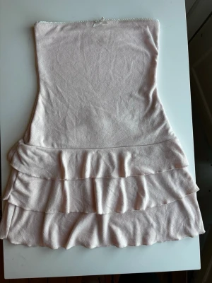 Ljusrosa axelbandslös klänning med volanger från Edikted i New York - Supersöt ljusrosa axelbandslös klänning med volangdetaljer i nederdelen och en liten rosett upptill. Mjukt material i bomull och polyester. Perfekt skick! Storlek S