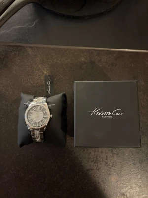 Kenneth Cole klocka - Säljer denna helt oanvända klocka åt min morfar. Klockan kommer från ett lager efter en nedlagd klockbutik och har aldrig använts.  * Skick: Ny/oanvänd * Funktion: Klockan saknar batteri, vilket köparen själv får ordna. * Box och tagg medföljer vid köp. * Nypris: cirka 2 000 kr.  Klockan säljs privat och kan skickas eller hämtas efter överenskommelse. Fler bilder kan skickas vid intresse.  Pris kan diskuteras vid snabb affär.