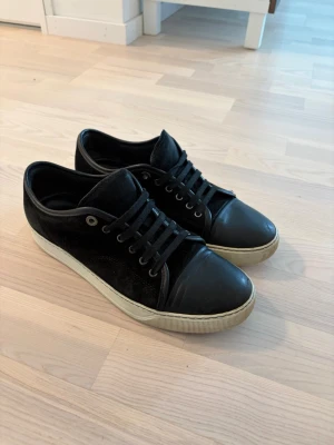 Svarta Lanvin Skor - Säljer ett par svarta Lanvins i låg modell med ovandel i mocka och tåparti i slätt läder. Skorna har svarta skosnören, metallöljetter och svart sula med diskret struktur. Perfekta för en clean och stilren look.