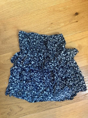 Volangkjol - Mörkblå volang kjol med vita blommor. Väldigt Stretchig i midjan så skulle säga att de passar alla storlekar från xs-m. Köpt i Grekland. 