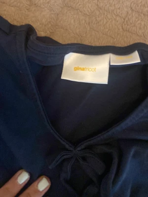 Mörkblå blus med puffärm Gina Tricot - Supersöt mörkblå blus från Gina Tricot med puffiga korta ärmar och knytning framtill. Blusen har en volang nertill som ger en flowy känsla. Perfekt att styla med jeans eller kjol för en trendig look.