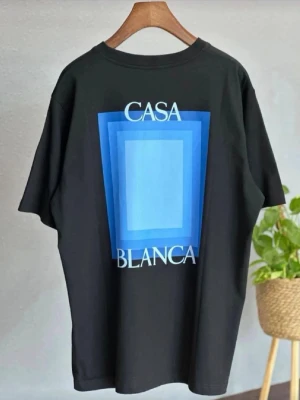 Casa. Blanca Svart t-shirt med blått tryck - Casa Blanca Snygg svart t-shirt med stort grafiskt tryck i olika blå nyanser och texten 'CASA BLANCA' på ryggen. Klassisk passform och rund halsringning. Perfekt för dig som gillar stilrena men ändå unika plagg. Pris kan sänkas 