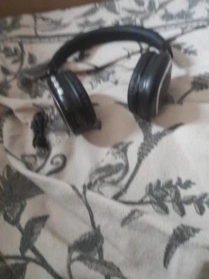 Svarta over-ear hörlurar med sladd - Säljer ett par svarta over-ear hörlurar med vadderad bygel och mjuka öronkuddar. Hörlurarna har en stilren design och medföljer en USB-laddningskabel. Perfekta för musik, gaming eller videosamtal.