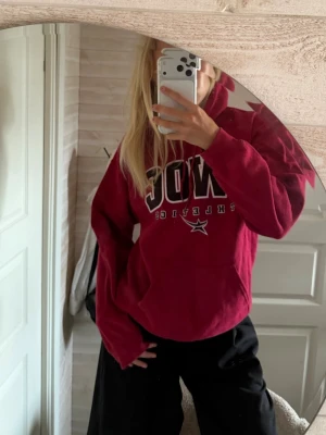 Mörkröd hoodie med tryck - Säljer en mörkröd hoodie med stor vit och svart text på bröstet och ryggtryck med flera loggor och texten GWOC. Hoodien har huva och känguruficka framtill. Perfekt för dig som gillar sportig och avslappnad stil.