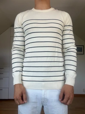 Beige tröja med mörkblå ränder - Beige och mörkblå randig stickad tröja tillverkad i 100% bomull. Tröjan är ifrån märket Pier One. Strl S. Inga defekter. Modellen är 178 cm och väger 77 kg. Hör gärna av dig vid frågor!