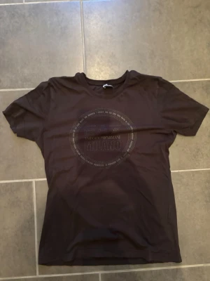 Svart EA7 Emporio Armani t-shirt - Snygg svart t-shirt från EA7 Emporio Armani med rund hals och ett stort tryck i silver på bröstet där det står EA7 Emporio Armani Milano. Perfekt för dig som gillar stilrena och exklusiva plagg.