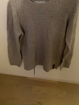 Beige stickad tröja - En enkel och stilren beige stickad tröja med rund halsringning och långa ärmar. Tröjan har en mjuk struktur och ribbade muddar vid ärmslut och nederkant. Perfekt för lager på lager och passar till det mesta.