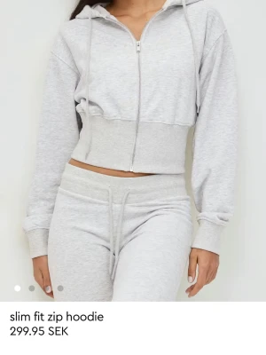 Ljusgrå kofta från Ginatricot - Ljusgrå hoodie i slim fit-modell med dragkedja framtill och huva med dragsko. Croppad längd och bred ribbad mudd i midjan ger en modern look. Tillverkad i mjukt sweatshirtmaterial som är perfekt för en avslappnad stil. Använd 2-3 gånger men känner inget behov att behålla den. Skicket är som nytt. 