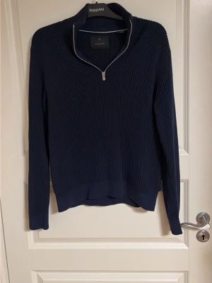 Mörkblå stickad tröja med dragkedja - Mörkblå stickad tröja från Jack & Jones med ribbad struktur och halv dragkedja vid halsen. Tröjan har lång ärm och hög krage som kan vikas ner. Perfekt för lager på lager och enkel att matcha till olika outfits.