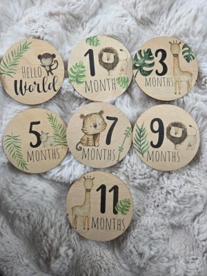 Träbrickor för baby månadsbilder - Säljer ett set med runda träbrickor för att fota bebisens utveckling varje månad. Brickorna har söta djurmotiv som lejon, giraff, elefant och apa samt gröna blad. Varje bricka har text för månad eller år och en för födelseinformation. Perfekt för att skapa minnen!