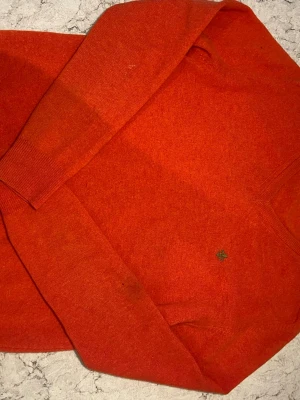 Orange stickad tröja från Morris - Snygg orange stickad tröja från Morris i 100% merinoull. Tröjan har rund halsringning med grön insida och diskret Morris-logga broderad framtill. Perfekt för lager-på-lager och håller dig varm under kyliga dagar.