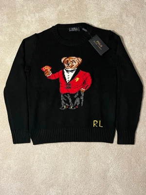 Svart stickad tröja Polo Ralph Lauren bear/björn  - Hej! Jag säljer en superfin stickad polo Ralph lauren tröja i storlek S i svart färg.  Denna tröja är perfekt till att hålla värmen, vilket gör den perfekt nu under kallare tider!  Mjuk och gosig stickad tröja som passar till hemmet, utomhus, eller vart som helst där man vill ha på sig en mjuk, varm och skön tröja!  Inget slitage på märket, kommer från djur och rökfritt hem. Tröjan har ingen konstig lukt. Tröjan kan passa både män och kvinnor!