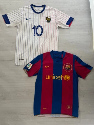 Mbappé och Ronaldinho fotbolls jersey paket. - Två fotbollströjor: en vit Frankrike-tröja med blå och röda ränder, blå detaljer och nummer 10 (Mbappé) samt en Barcelona-tröja i blått och vinrött med gula detaljer, UNICEF-logga och nummer 10 (Ronaldinho).