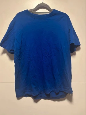 Blå basic t-shirt i bomull - En enkel blå t-shirt med rund hals och korta ärmar. Tillverkad i mjuk bomull och har en klassisk passform. Perfekt till jeans eller shorts för en avslappnad look.