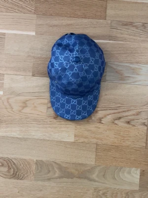 Blå keps från Gucci med monogram - Säljer en blå keps från Gucci med det klassiska GG-monogrammet över hela kepsen. Kepsen har böjd skärm och justerbar rem bak. Materialet är denimliknande tyg som ger en cool och trendig look.