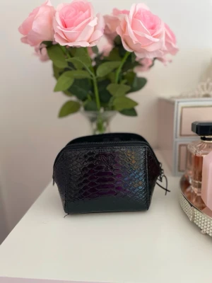 Victoria’s Secret sminknecessär   - Säljer en svart sminknecessär från Victoria’s Secret med reptilmönster och glansig finish. Perfekt för att förvara smink och stilren design som passar i handväskan. 
