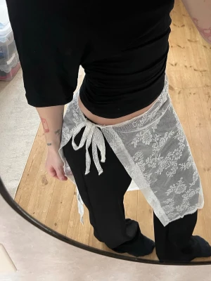 Vit omlottkjol i spets med knytband - Säljer en vit handsydd omlottkjol i spets med knytband i midjan. Kjolen är kort och har ett blommigt spetsmönster som ger en romantisk vibe. Perfekt att styla över jeans eller byxor för en trendig lager-på-lager-look. Passar S/M. 