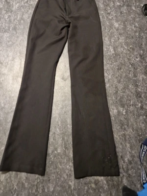 Svarta utsvängda kostymbyxor - Snygga svarta kostymbyxor med utsvängda ben och klassisk passform. Byxorna har hög midja och stängs med dragkedja och knapp. Perfekta för en stilren look. Materialet är slätt och ger en dressad känsla.