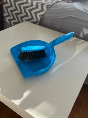 Blå sopborste och skyffelset - Säljer ett blått sopborste och skyffelset i plast. Borsten har svarta strån och ett ergonomiskt handtag med hål för upphängning. Perfekt för att snabbt sopa upp smulor och damm i hemmet. Lätt att förvara och använda i köket, hallen eller sovrummet.