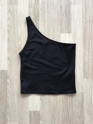 Svart oneshoulder topp från Gina Tricot, stl S - Snygg svart oneshoulder topp med enkel och stilren design, från Gina Tricot. Ribbat tyg. Perfekt att matcha med både jeans och kjol. Just nu fri frakt, så du betalar bara för toppen. Jag har fler plagg ute, och hittar du något mer från min garderobsutrensning, så skickar jag i samma paket.