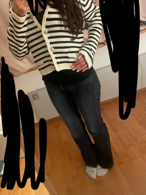 Randig stickad kofta med guldknappar - Snygg stickad kofta i vitt med svarta horisontella ränder och guldiga knappar framtill. Kort modell med långa ärmar och ribbade muddar. Perfekt för att lyfta din outfit med en trendig touch.