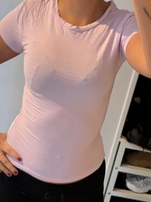 Ljusrosa tight t-shirt i bomull - En enkel och snygg ljusrosa t-shirt med tight passform och rund halsringning. T-shirten är kortärmad och gjord i mjuk bomull, perfekt för dig som gillar en clean och stilren look. Passar till jeans, shorts eller joggers.