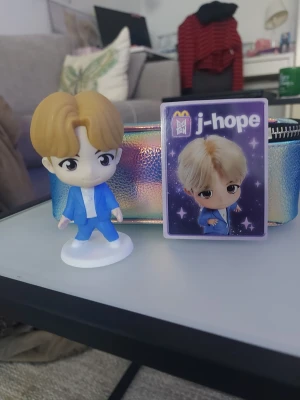 J-Hope figur och samlarkort - Säljer en J-Hope figur i blå kostym med vit skjorta, samt ett samlarkort med J-Hope från McDonald's BTS-kampanj. Perfekt för fans av K-pop och BTS. Figuren är gjord av plast och står på en vit platta. Kortet har lila bakgrund med stjärnor.