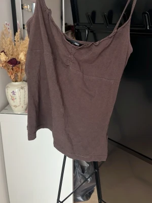 Brun linnetopp från H&M - Säljer en enkel brun linnetopp från H&M med smala axelband och avslappnad passform. Perfekt att styla med jeans eller kjol för en chill look. Materialet känns mjukt och lätt mot huden.