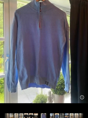 Blå halvziptröja från New Zealand Auckland - Ljusblå stickad tröja med halv dragkedja från New Zealand Auckland. Tröjan har ett diskret mönster, ribbade muddar och en patch med logga på ärmen. Perfekt för en avslappnad men snygg stil.