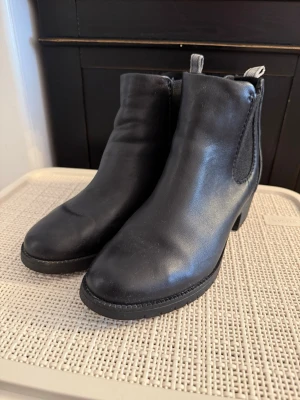 Hadley Svarta chelsea boots från Hush Puppies - Stilrena svarta chelsea boots från Hush Puppies i skinn med elastiska paneler på sidorna och låg klack. Klassisk rund tå och dragflik bak för enkel påtagning. Perfekta till både jeans och kjol för en clean look. I fint skick då jag knappt använt dem. Lätta boots