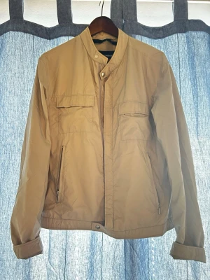 J.lindeberg Jacka - Stilren beige J. Lindeberg jacka. Perfekt för svala dagar och enkel att matcha med olika outfits. Denna jacka är en tidigare version av J.Lindebergs klassiska Bailey-modell i Nylon. I utmärk skick.
