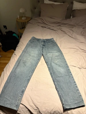 Ljusblå raka jeans - Säljer ett par ljusblå jeans med rak passform och klassisk femficksdesign. Jeansen har hög midja och är tillverkade i denim. Perfekta för en avslappnad och trendig stil. Har sytt upp dom så dom är 27/30