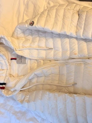 Vit dunjacka från Moncler med huva - Snygg vit dunjacka från Moncler med huva och dragkedja framtill. Storlek 2 passar som S/M.  Fläck vid dragkedjan varav det billiga priset. Slå ett PM för fler bilder, pris går att diskuteras. 