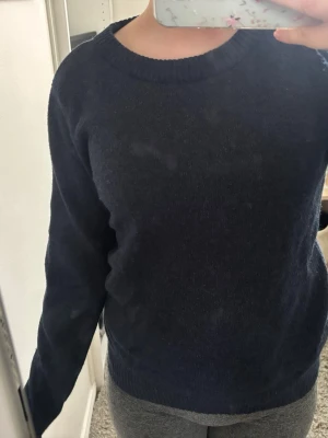 Mörkblå stickad tröja - En enkel och stilren mörkblå stickad tröja med rund halsringning och långa ärmar. Tröjan har ribbstickade muddar vid hals, ärmslut och nederkant. Perfekt för lager-på-lager och passar till det mesta. Använd 1 gång så inte nopprig