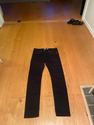 Svarta slim fit jeans från Calvin Klein - Säljer ett par svarta slim fit jeans från Calvin Klein med klassisk femficksdesign och diskret logotyp på bakfickan. Jeansen har raka ben och är tillverkade i ett stretchigt material som ger en skön passform. Byxorna har en lite fläck på en knät men märks inte av så värst, skulle säga att den är mindre än storleken säger. Byxorna har en lite fläck på ena knät men annars är dom prima skick.