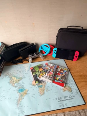 Nintendo Switch med spel och tillbehör  - Nintendo Switch spelkonsol med en blå Joy-Con på vänster sida och en röd Joy-Con på höger sida. Konsolen har en stor skärm i mitten och är tillverkad i plast. Perfekt för gaming på språng eller hemma. Tre spel medföljer: Super Smash Bros Ultimate, Super Mario Odyssey och Luigi's Mansion 3. Två racing wheel kontroller och en pro controller med en liten och en stor väska för konsolen. Pris går att diskuteras 